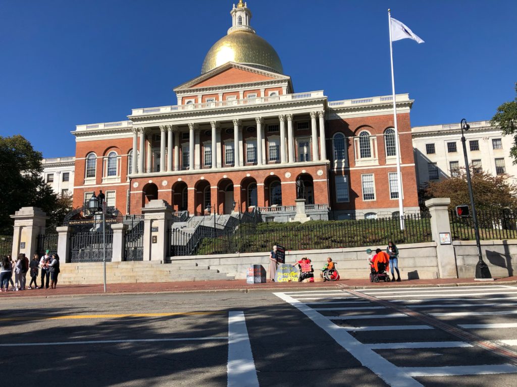 Disabled protesters holding signs in front of the Massachusetts State House