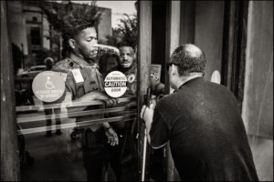 ADAPTer with a cane trying to open a door, while police officers try opening the door for them