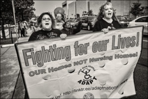 Two ADAPTers holding a poster saying “Fighting for our Lives! OUR Homes NOT Nursing Homes!”