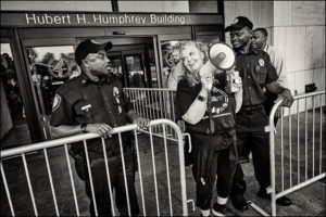 ADAPTer with megaphone standing with police officers in front of Health and Human Services.