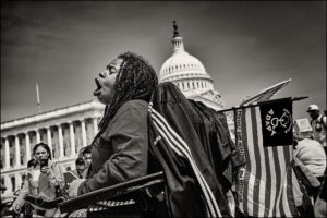 ADAPTer in wheelchair holding ADAPT American flag and yelling in front of the Capitol