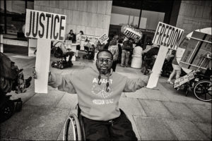 ADAPTer in wheelchair holding two signs saying “Justice” and “Freedom”